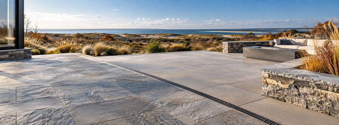 Coastal East End terrace combining natural stone and large-format pavers with visible drainage near the dunes